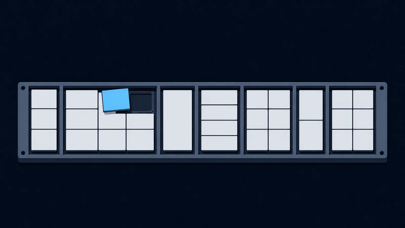 A wide sorting plate of seven unequal bays holding blank tiles, with one tile lifted clear.